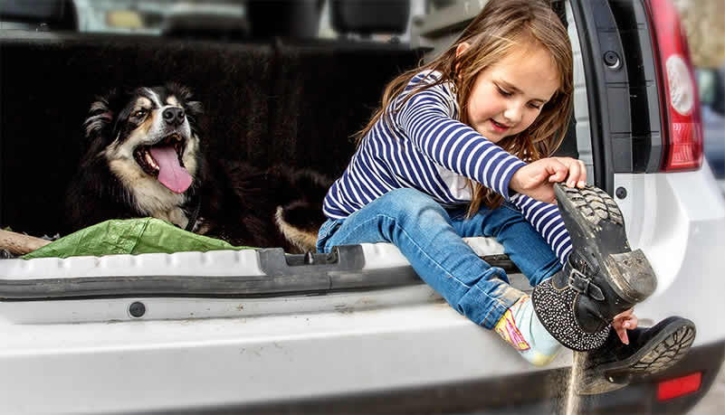 Cute girl taking off sandy boots in the back of an SUV with her dog